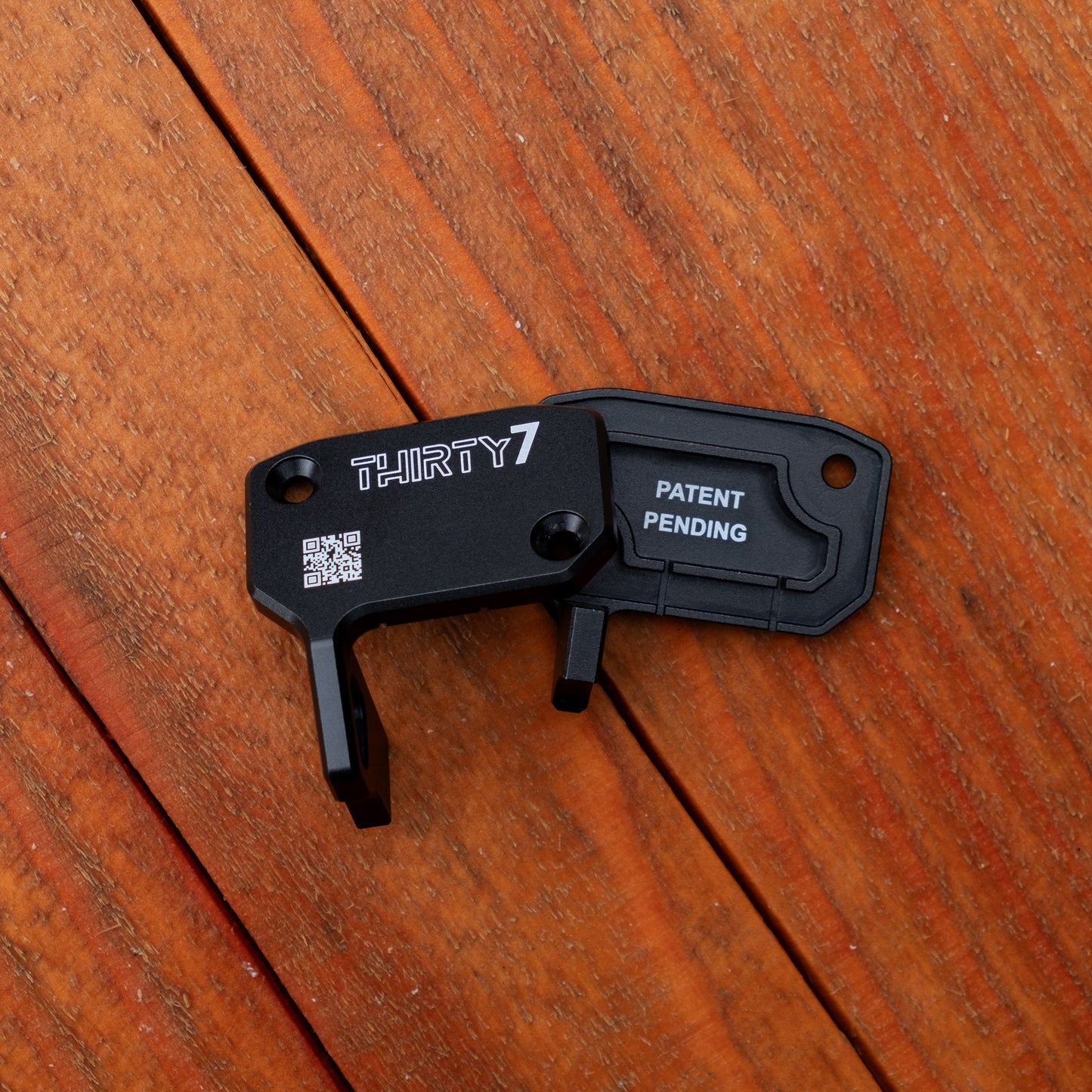 A black metal lock pick tool with 'THIRTY7' and 'PATENT PENDING' printed on it, resting on a brown wooden plank surface.